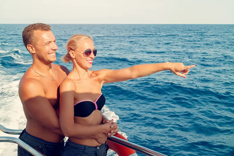 A luxury adult-only cruise ship sailing into the sunset with couples socializing on deck.
